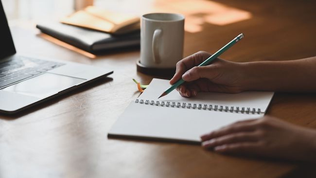 Photo of a person's hands writing in a notebook.