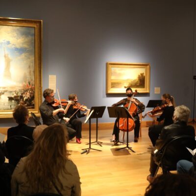 Photo of chamber musicians performing next to paintings at Minnesota Marine Art Museum.