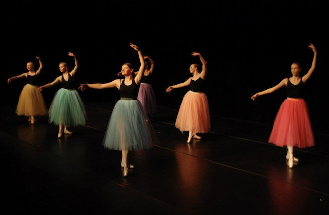 Photo of several ballet dancers wearing black tops and tutus in various colors.