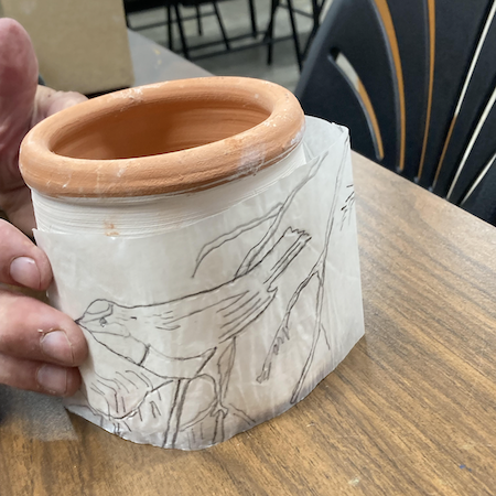 Image of a pottery crock with a bird design being applied on a paper slip.