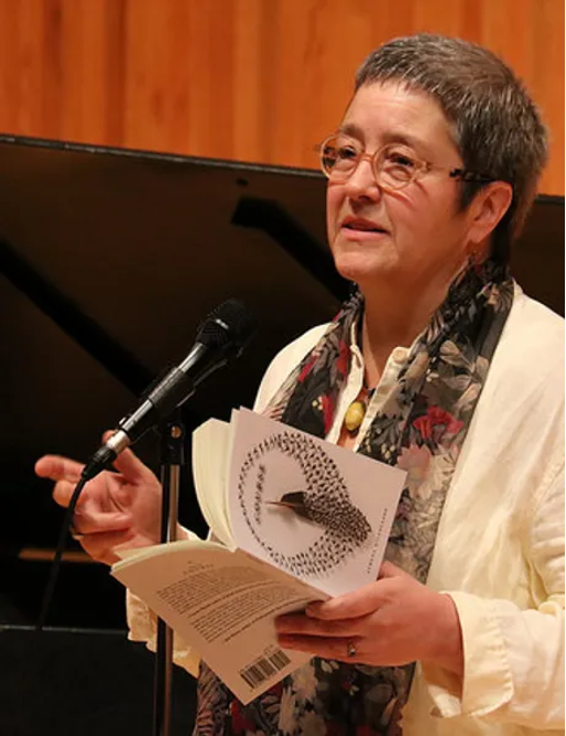 Photo of Athena Kildegaard reading from a book at a microphone.