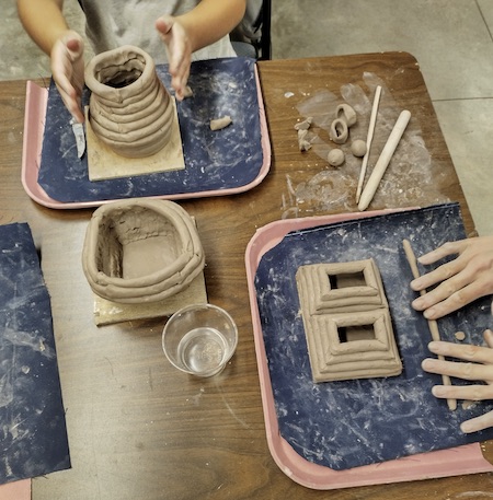 Photo of two people's hands making coiled clay pots.