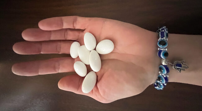 Photo of hand holding several white seeds or stones, and wearing a blue bracelet.