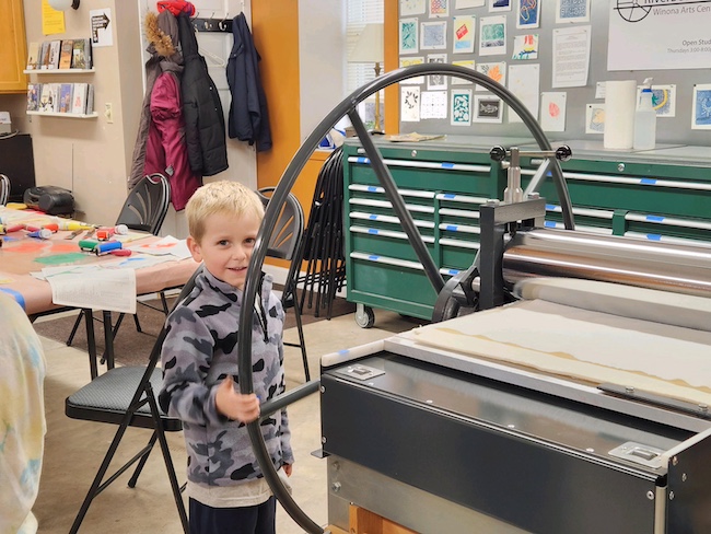 Photo of a child spinning the wheel of the printing press at Winona Arts Center.