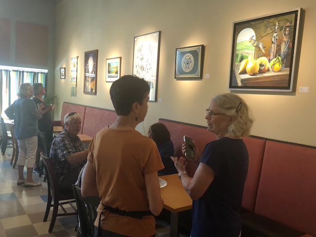 People talking and looking at artwork on the wall at the Blue Heron Coffeehouse.