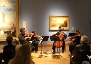 Photo of chamber musicians performing next to paintings at Minnesota Marine Art Museum.