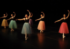 Photo of several ballet dancers wearing black tops and tutus in various colors.