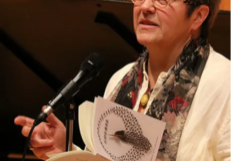 Photo of Athena Kildegaard reading from a book at a microphone.