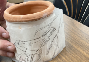 Image of a pottery crock with a bird design being applied on a paper slip.